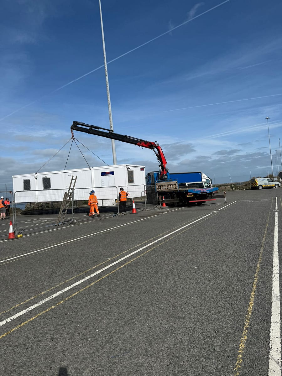 RN Roberts rigid HIAB lorry using its crane to lift a large welfare cabin